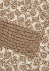 Tkanina smeše smeđe i krem boje s teksturiranim uzorkom; sadrži rebrasti smeđi manžet. Uzorak uključuje suptilne akcentne metalne niti.