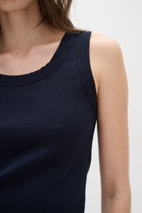 Temno modra rebrasta majica brez rokavov s širokim okroglim izrezom, brez rokavov in mehkim otipom; prilegan silhueta, ki prikazuje obliko telesa.