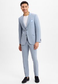 Lichtblauw kostuum met een gestructureerde afwerking, enkel-breasted jas, notch revers en een lichtblauwe pochet. Gecombineerd met donkere schoenen.