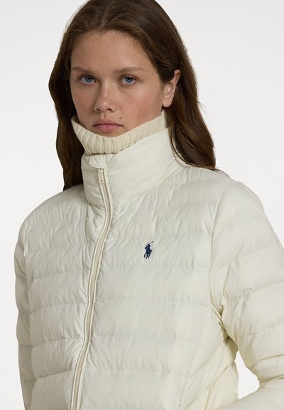 Ivory puffer jacket with a high collar and subtle ribbed texture; features a front zipper and small navy logo on the left chest.