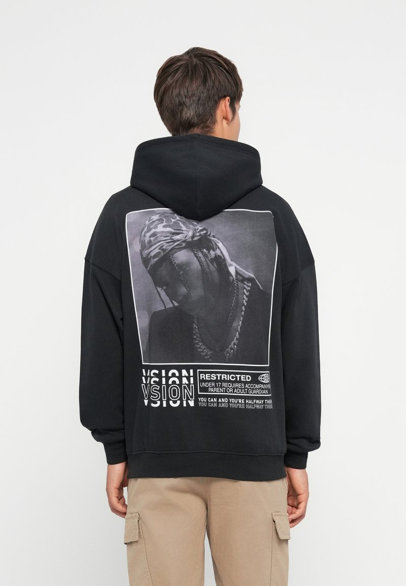 Μαύρη κουκούλα με μεγάλο γραφικό σχέδιο στο πίσω μέρος, που απεικονίζει ένα πορτρέτο και κείμενο. Υλικό από βαμβάκι με ριμπ μανσέτες και στρίφωμα.