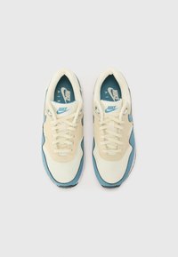 Nike Air Sneaker mit einem cremefarbenen Mesh-Obermaterial und blauen Akzenten, runder Zehenform, flachen Schnürsenkeln und einer strukturierten Gummisohle.
