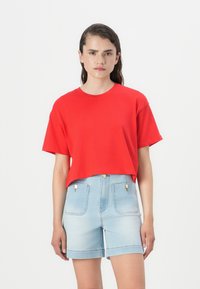 Raudona trumpa t-shirt marškinėliai su trumpomis rankovėmis, derinami su šviesiai mėlynomis džinsinėmis šortais, turinčiais du priekiniai kišenes ir auksiniais detalėmis.