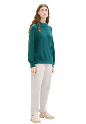 Türkiser gerippter Pullover mit hohem Kragen und langen Ärmeln, kombiniert mit hellgrauen, locker sitzenden Hosen und beigen Plattformslippern.