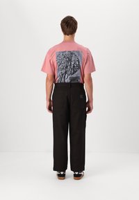 Roze t-shirt met een zwarte bloemenprint op de achterkant, gecombineerd met een ruimvallende bruine broek met zijzakken en een gestructureerde afwerking.