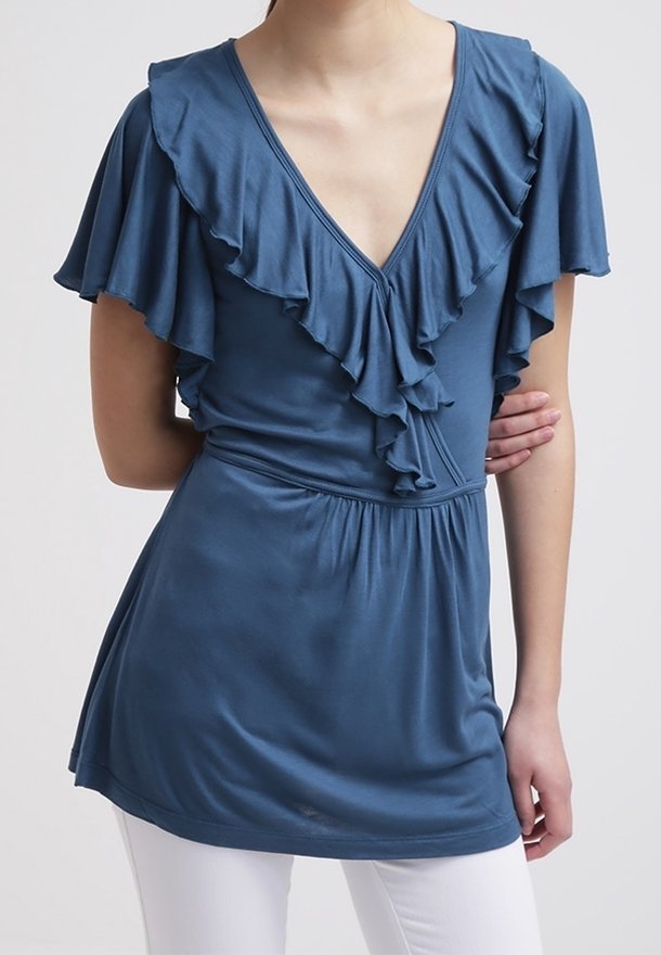 Niebieska bluzka z krótkim rękawem, z głębokim dekoltem w kształcie litery V i falbaniastymi detalami wzdłuż dekoltu oraz rękawów. Miękka tkanina z marszczonym pasem.