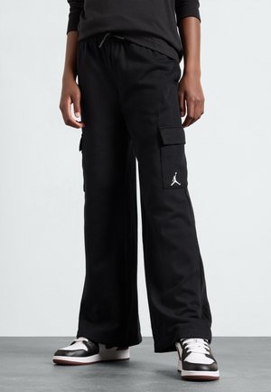 Zwarte cargobroek gemaakt van zachte stof, met een losse pasvorm, zijzakken en een wit logodetail. Gecombineerd met zwart-witte sneakers.