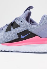 Zapatilla de running de Nike con parte superior de malla en un púrpura claro, acentos negros, entresuela rosa y suela de goma texturizada para agarre. Presenta un logo en azul.