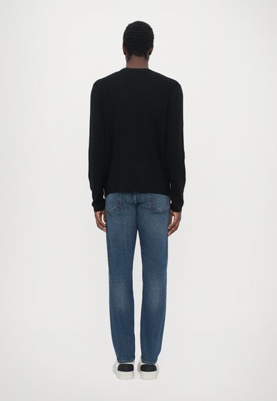 Un pull noir à manches longues associé à un jean droit bleu, présentant une texture lisse, une coupe standard et un design minimaliste.