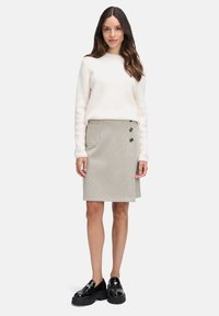 Beżowy sweter o fakturze i spódnica w kratę z dwoma dekoracyjnymi guzikami oraz kieszonką z boku. Czarny platformowy obuwie dopełnia strój.