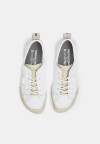 Baskets blanches avec une tige en mesh, des accents en suède beige et des lacets beiges. Présente des logos sur la languette et le talon, semelles plates.