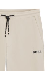 Beige sweatpants made of textured fabric, featuring a black drawstring and side pockets. "BOSS" logo in black on the lower side.