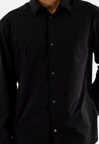Camisa negra de manga larga con botones, hecha de una tela suave y ligera, con un cuello clásico y seis botones a juego en el frente.