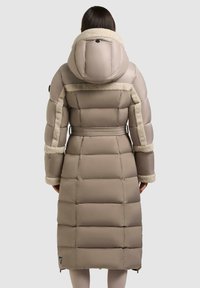 Cappotto lungo e imbottito in beige con cappuccio foderato in pelliccia sintetica, con cintura in vita, caratterizzato da un tessuto liscio e dettagli di trapuntatura orizzontale.
