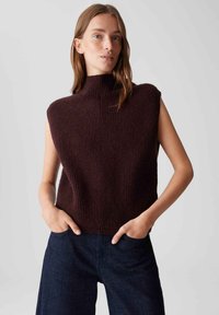 Gebreide mouwloze hoge hals top in donkerbordeaux met geribbelde textuur, met een boxy pasvorm en hoekig schouderontwerp. Gecombineerd met donkere spijkerbroek.