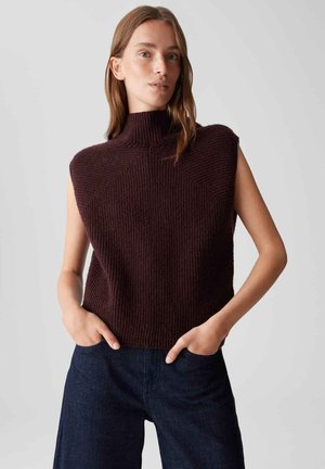 Gebreide mouwloze hoge hals top in donkerbordeaux met geribbelde textuur, met een boxy pasvorm en hoekig schouderontwerp. Gecombineerd met donkere spijkerbroek.