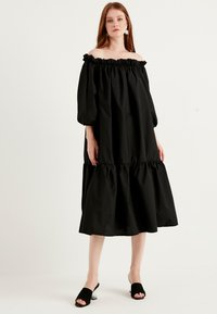 Svart off-shoulder klänning med volangkant i halsen, trekvarts puffärmar, lagrad nederdel och slät bomullstextur.