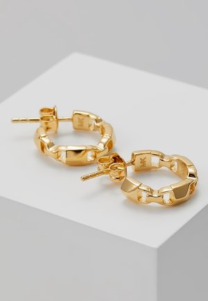 Petites boucles d’oreilles créoles dorées avec un design de chaîne liée et des attaches à tige, reposant sur une surface géométrique blanche.