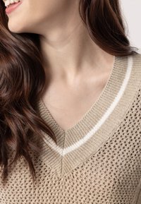 Maglione beige lavorato a maglia con scollo a V e strisce bianche sul colletto, caratterizzato da una trama morbida e una tessitura leggera che si adagia sulle spalle.
