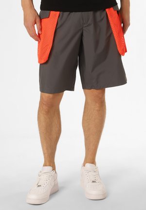 Graue Shorts mit einem leichtgewichtigen Design, ausgestattet mit großen, orangefarbenen Netztaschen an beiden Seiten. Getragen mit weißen Sportschuhen.