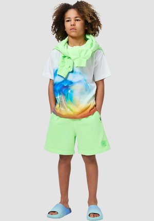 Weißes T-Shirt mit kurzen Ärmeln und blau-orangefarbenem Farbverlauf, kombiniert mit neongrünen Shorts. Grüner Hoodie um den Hals gebunden und blaue Slide-Sandalen.