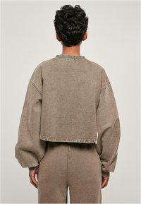 Kuttet, brun hettegenser med store ermer, ribbestrikkede mansjetter og flat halslinning. Laget av myk teksturert stoff med et ensfarget design.