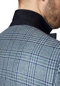 Marynarka w niebiesko-zielony wzór houndstooth z ciemnym, teksturowanym kołnierzem i delikatnymi detalami w postaci szwów, podkreślająca dopasowany krój.