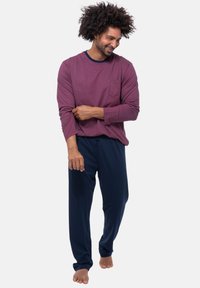 Maglietta a maniche lunghe bordeaux con collo a giro e taschino, abbinata a pantaloni blu navy con cordino in vita. Tessuto morbido con vestibilità rilassata.