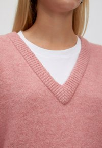 Roze gebreide trui met een V-hals en geribbelde kraag, gedragen over een witte blouse, met een zachte, textuurrijke stof.