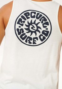 Camiseta sin mangas blanca con un gran logo circular negro que contiene el texto "Rip Curl Surf Co" y un gráfico de sol en el centro. Tejido suave y ligero.