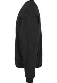 Sweat-shirt noir à manches longues vu de profil, avec poignets et bas côtelés et un col rond.
