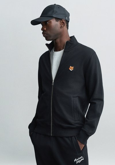Zwarte rits sweatshirt van een katoenmix, met een klein vospatch op de borst en zijzakken. Gecombineerd met zwarte sweatpants.