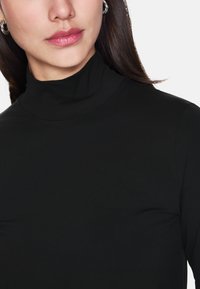 Schwarzes Rollkragenoberteil aus weichem, dehnbarem Stoff, mit einer figurschmeichelnden Silhouette und hohem Kragen. Einfaches Design ohne sichtbare Muster oder Beschläge.