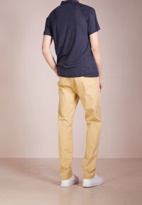 Navy short-sleeve shirt, yellow chinos, and white sneakers. The shirt has a relaxed fit, while the chinos feature a straight-leg design.