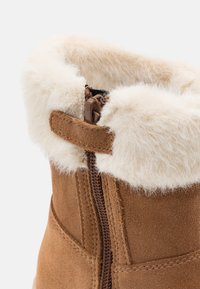 Ruskean mokkanahkasaappaat, joissa on pörröinen kerma värinen tekokarvaremmi, sivuvetoketju ja tikattu yksityiskohta reunoilla.