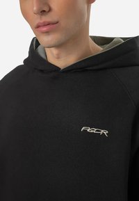 Zwarte hoodie met een zachte textuur, voorzien van een grijze binnenvoering en een klein geborduurd logo op de linkerkant van de borst.