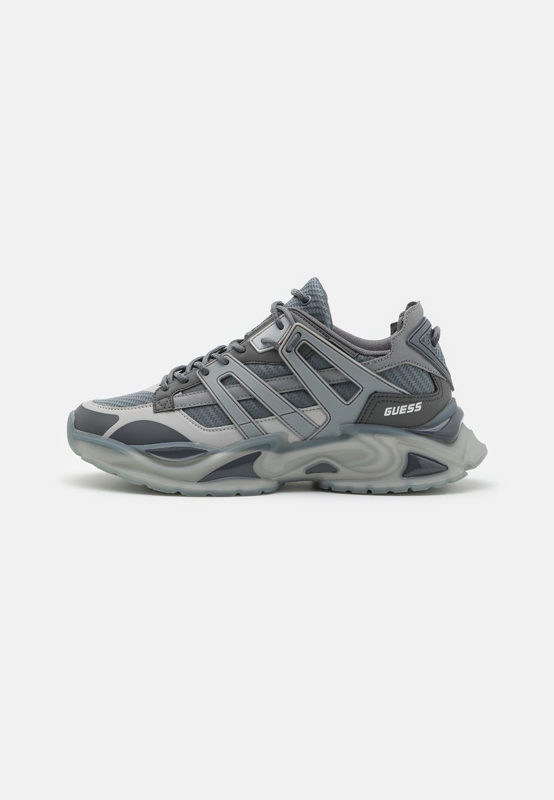 Chaussure de sport grise en matériau mesh et synthétique, dotée d'une semelle épaisse et texturée, d'accents diagonaux et d'un logo sur le côté.