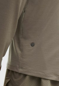 Hosszú ujjú világosbarna ing, puha anyagból készült. Diszkrét logóval és lapos varratokkal a szegélyén, alatta pöttyös rövidnadrággal.