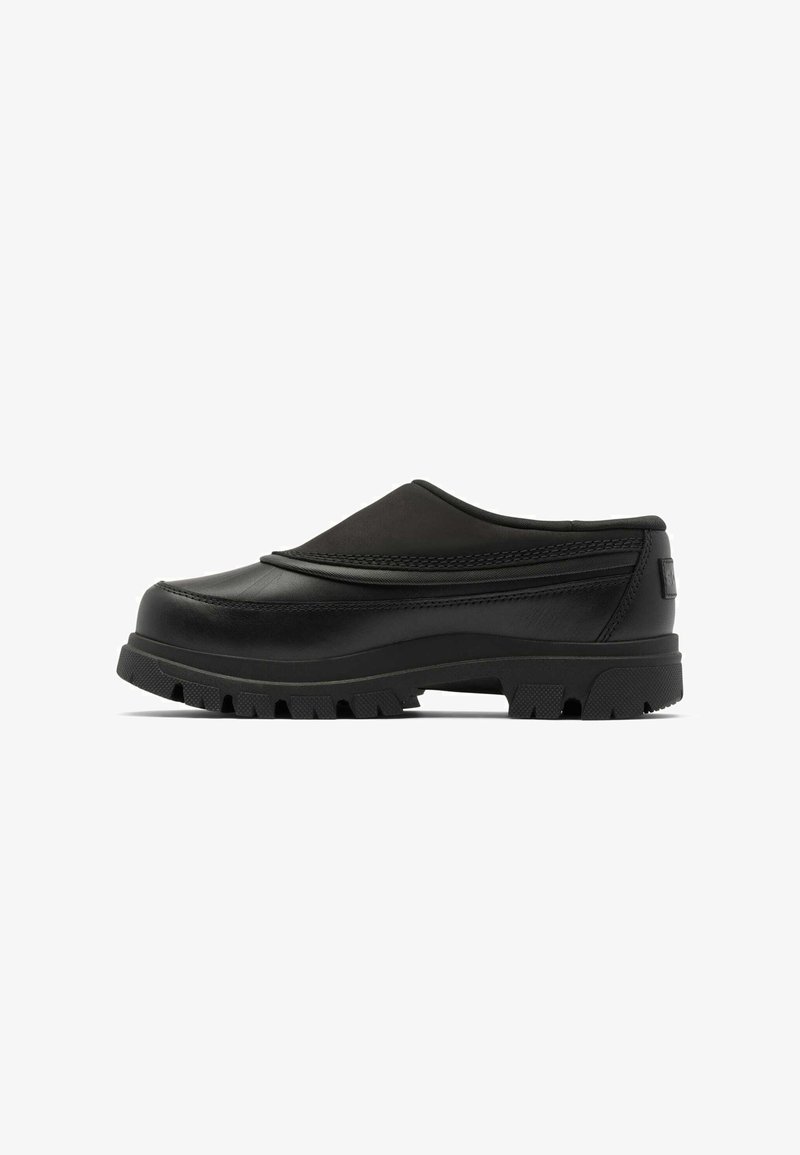 Schwarzer Slip-On-Schuh mit robustem Gummisohlen und strukturiertem Profil, niedrigem Absatz und gepolstertem Kragen, seitlich auf weißem Hintergrund gezeigt.