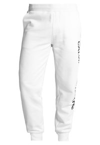 Białe spodnie dresowe wykonane z miękkiego materiału z prążkowanym pasem, z czarnym nadrukiem logo biegnącym pionowo wzdłuż lewej nogawki.
