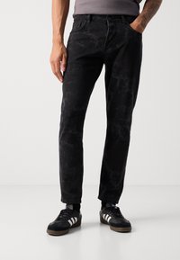Black denim jeans with a marbled texture, five pockets, and a slim fit. Paired with black sneakers featuring white stripes.