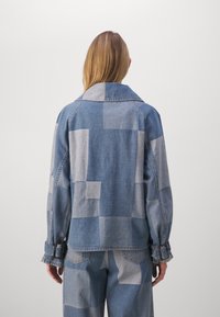 Denim jacket with a patchwork design in dark and light blue tones. Features a classic collar and cuffed sleeves.