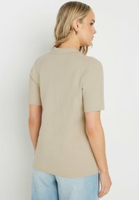 Haut beige à manches courtes avec un col, réalisé en tissu lisse. Présente un design ajusté et est associé à un jean bleu clair.