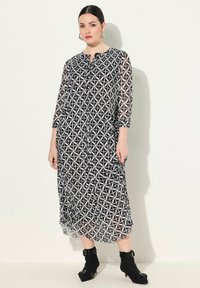 Robe longue noir et blanc à motifs géométriques, avec fermeture à boutons, manches trois-quarts et texture translucide. Associée à des bottines.