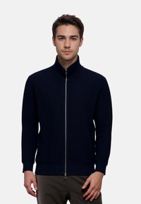 Navy ribbed knit zip-up sweater with a high collar and long sleeves, featuring a silver zipper and textured fabric.