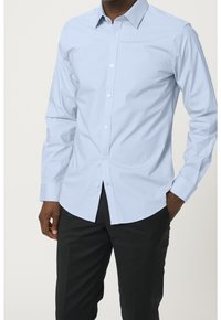 Ljusblå långärmad skjorta i bomull, knäppning fram, mjuk textur, strukturerad krage, med en figursydd silhuett och svarta byxor.