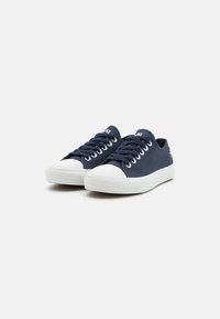 Marineblå kanvas sneakers med hvite gummisåler, rund tå og hvite lisser. Har en logo på siden og teksturert såle for grep.