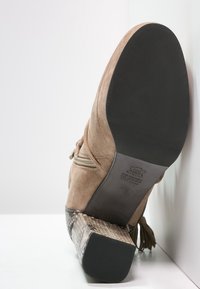 Stivaletto in suede marrone con suola nera, zip laterale e tacco a blocco, caratterizzato da un motivo in pelle di serpente, mostrato dal basso e da un'angolazione laterale.