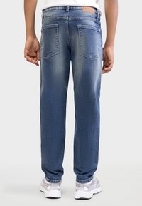 Τζιν παντελόνια από denim σε μέτριο μπλε ξέβγαλμα με ξεθωριασμένες λεπτομέρειες. Διαθέτει τσέπες και ραφές σε κανονικό μέγεθος· ίσια γραμμή ποδιού και διακριτή υφή.