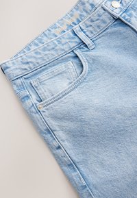 Jean en denim bleu clair avec une surface texturée, doté d'une poche avant, de ferrures argentées et d'une étiquette à la taille "denim supply".